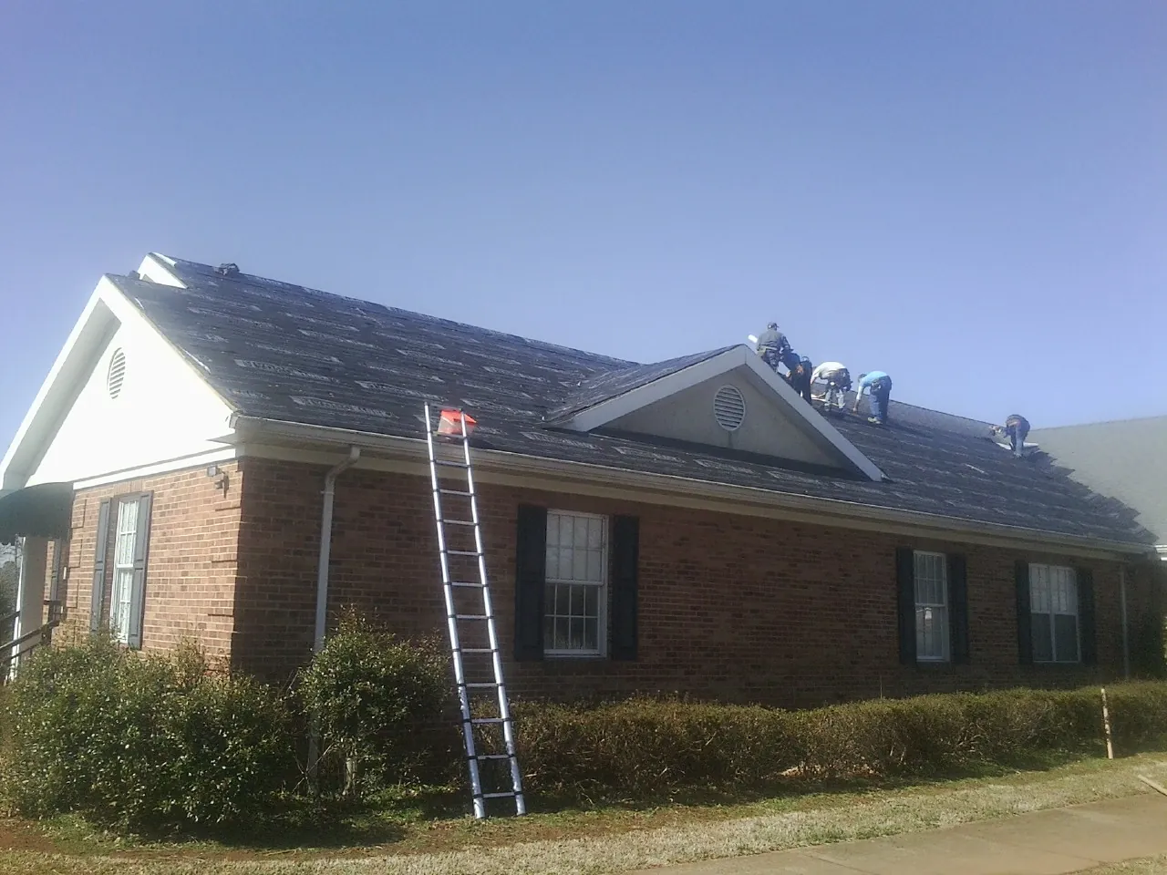 Crew tearing shingles off a brick ranch roof with a ladder set — Metal Roof Repair work by our crew in Kiowa