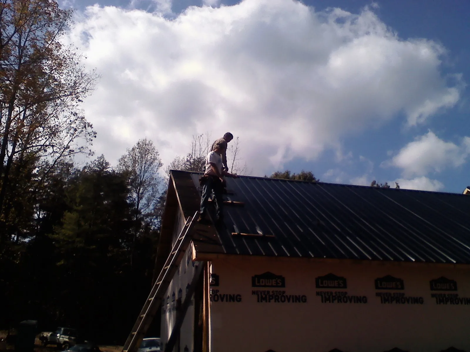 Roofer fastening dark metal panels high against a cloudy sky, from a Roof Inspection job in Kiowa