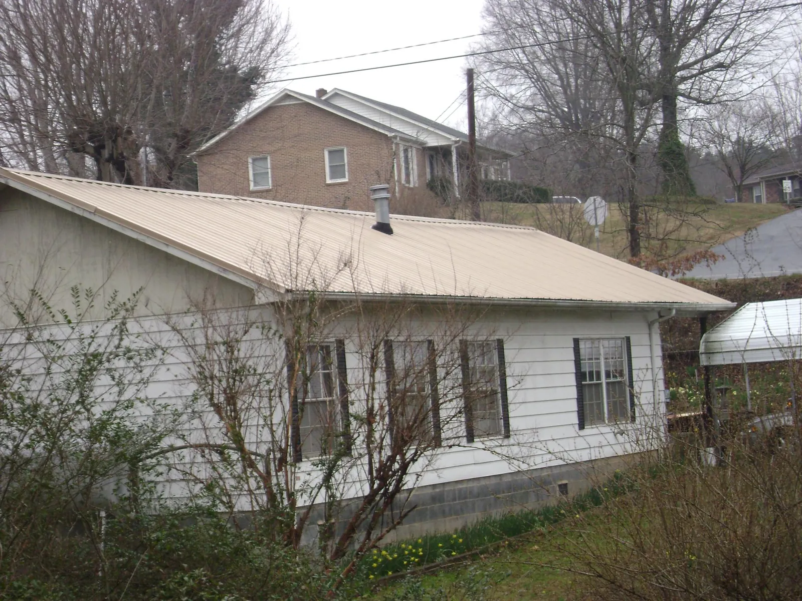 Tan metal roof on a white sided house set into a hillside — Commercial Roofing by Roofing Brothers in Kiowa